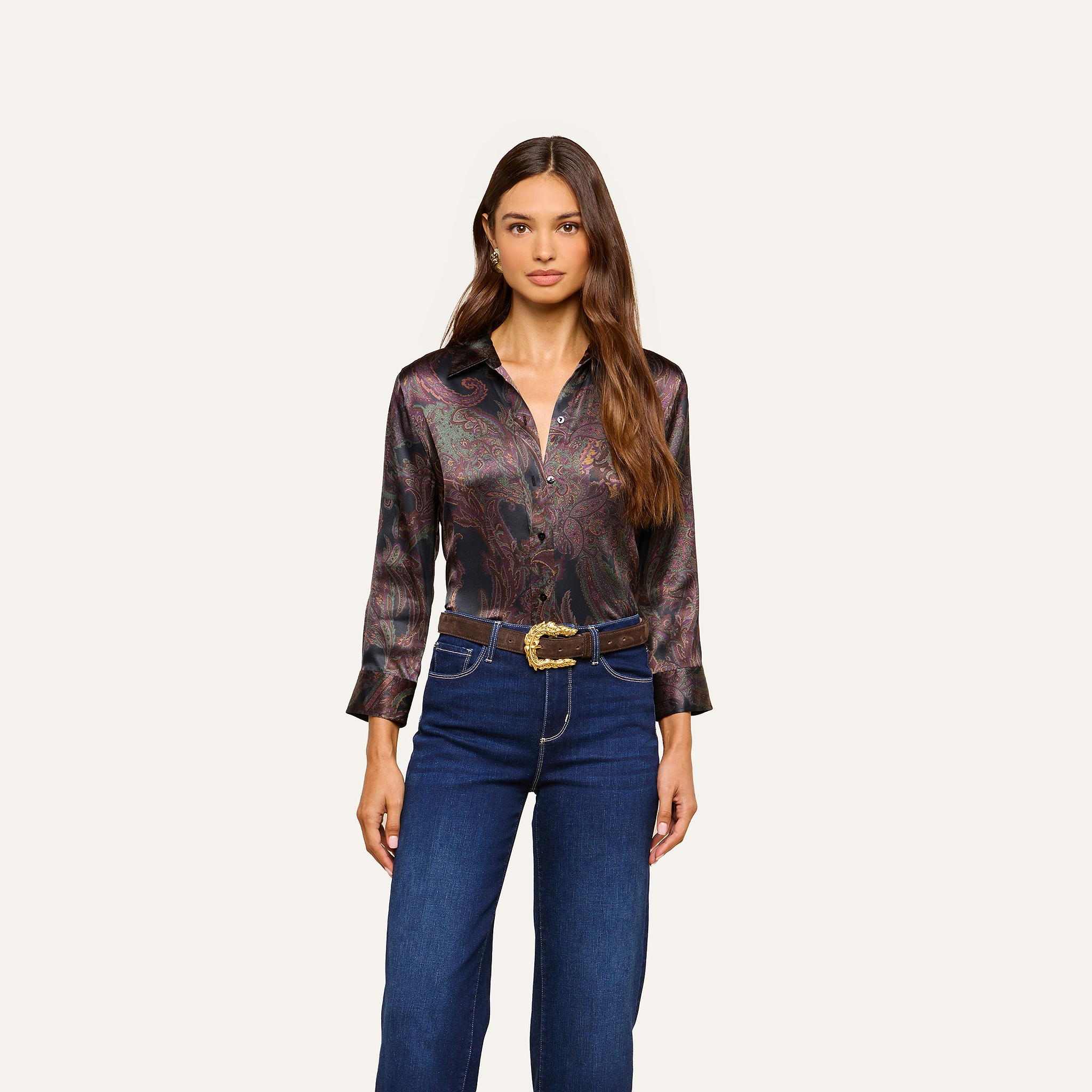 Woman with long brown hair wears the Dani Silk Blouse—a dark paisley shirt with three-quarter sleeves—paired with blue jeans and a decorative belt, standing against a plain off-white background.