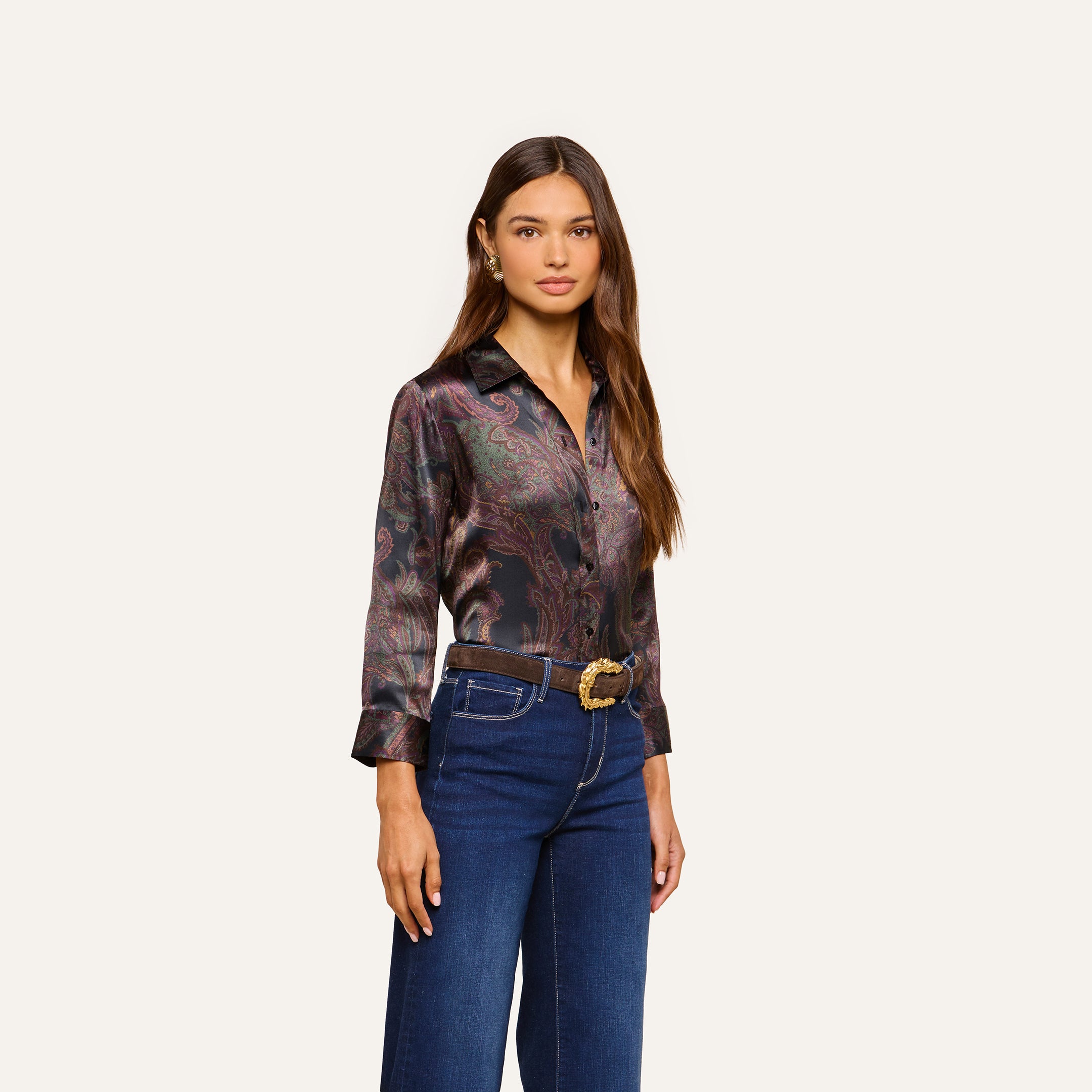 A woman with long brown hair stands against a plain light background, wearing the Dani Silk Blouse with three-quarter sleeves, tucked into high-waisted blue jeans with a belt.