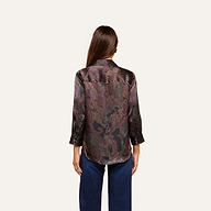 A woman with long brown hair, seen from the back, wears the Dani Silk Blouse—a dark paisley top with three-quarter sleeves—paired with blue jeans against a plain light background.