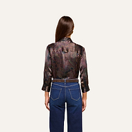 A person with long brown hair, seen from behind, wears the Dani Silk Blouse with rolled sleeves and blue jeans featuring prominent pockets against a plain light background.