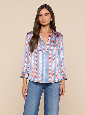A woman with long brown hair and a neutral expression stands against a beige background wearing the vertically striped Dani Silk Blouse with rolled sleeves and blue jeans.