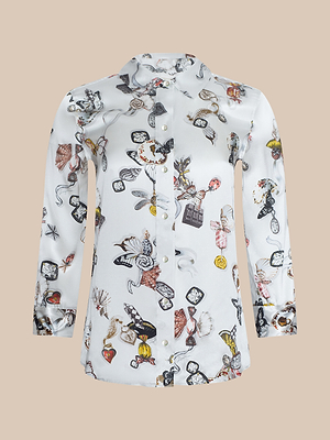 The Dani Silk Blouse is a long-sleeve button-down with a ruffled collar, showcasing a colorful whimsical print of watches, keys, flowers, and hearts on a light background.