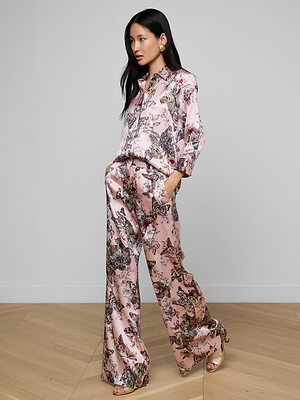 A woman stands indoors wearing the Dani Silk Blouse in a butterfly jungle print of pink, purple, and black. She poses confidently with one hand in her pocket against a plain background.