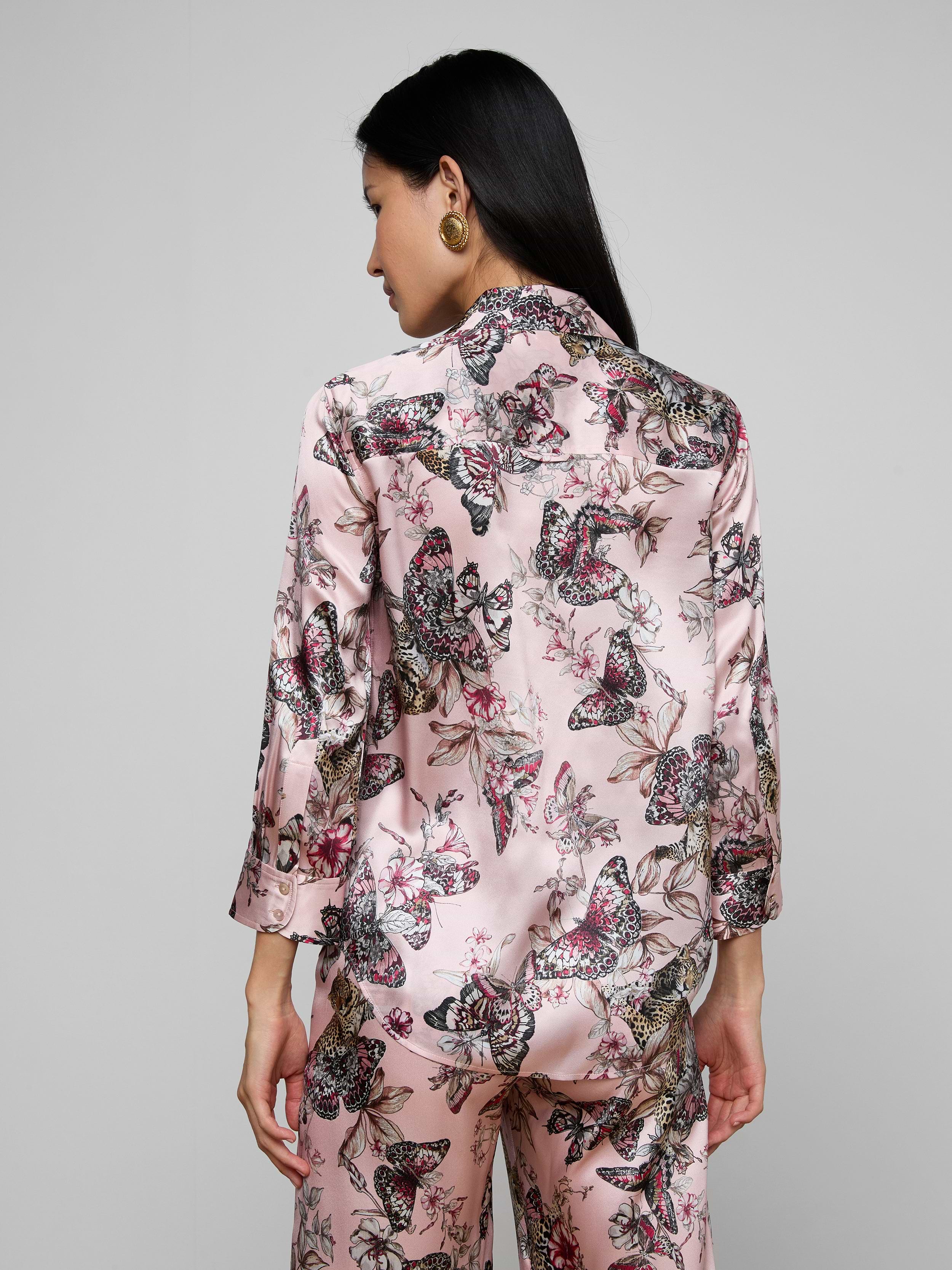 A woman with long dark hair, seen from the back, wears the Dani Silk Blouse featuring a pink butterfly jungle print, standing against a plain light background.