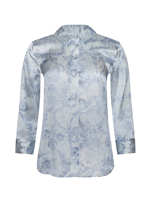 The Dani Silk Blouse features light blue satin, long sleeves, a classic collar, and a subtle floral pattern. This button-down shirt is shown against a white background.