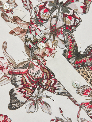 Close-up of the Dani Silk Blouse featuring a detailed butterfly jungle print in red, black, and beige. The image also highlights the white shirt placket with small white buttons.