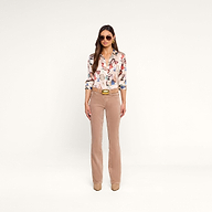 A woman wearing sunglasses, a Dani Silk Blouse featuring a vintage glassware print, beige straight-leg pants, a belt, and beige shoes stands against a plain white background.