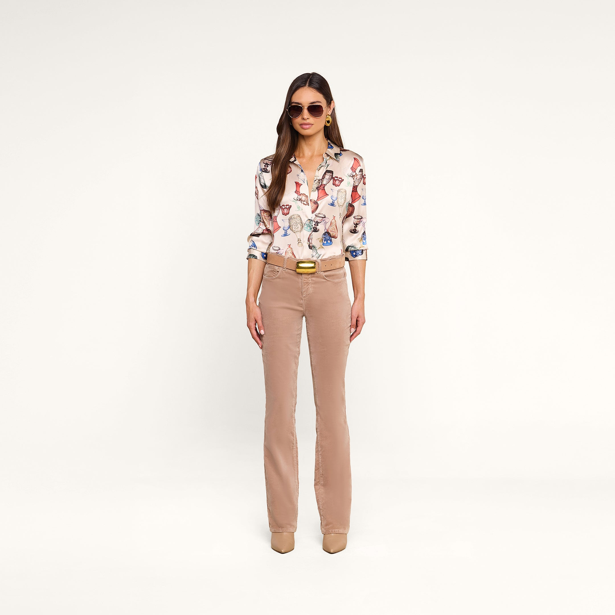 A woman wearing sunglasses, a Dani Silk Blouse featuring a vintage glassware print, beige straight-leg pants, a belt, and beige shoes stands against a plain white background.