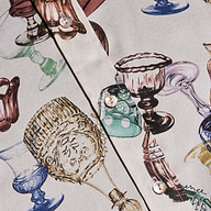 A close-up of the Dani Silk Blouse highlights a vibrant pattern of vintage glassware print goblets and cups, with pearly buttons adorning the front.