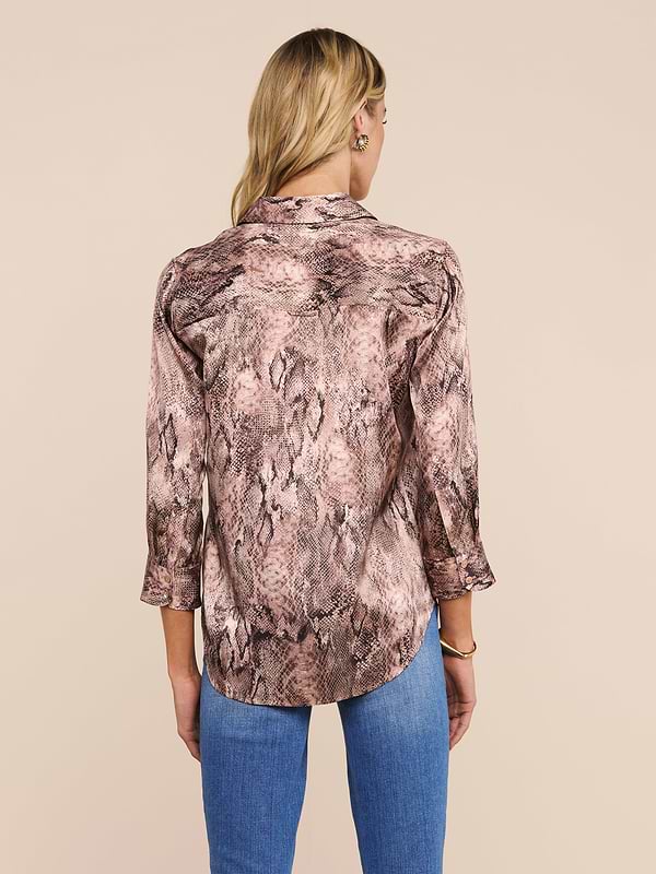 A person with long blonde hair is shown from the back against a plain, light background, wearing the Dani Silk Blouse—a snake print top with three-quarter sleeves—paired with blue jeans.