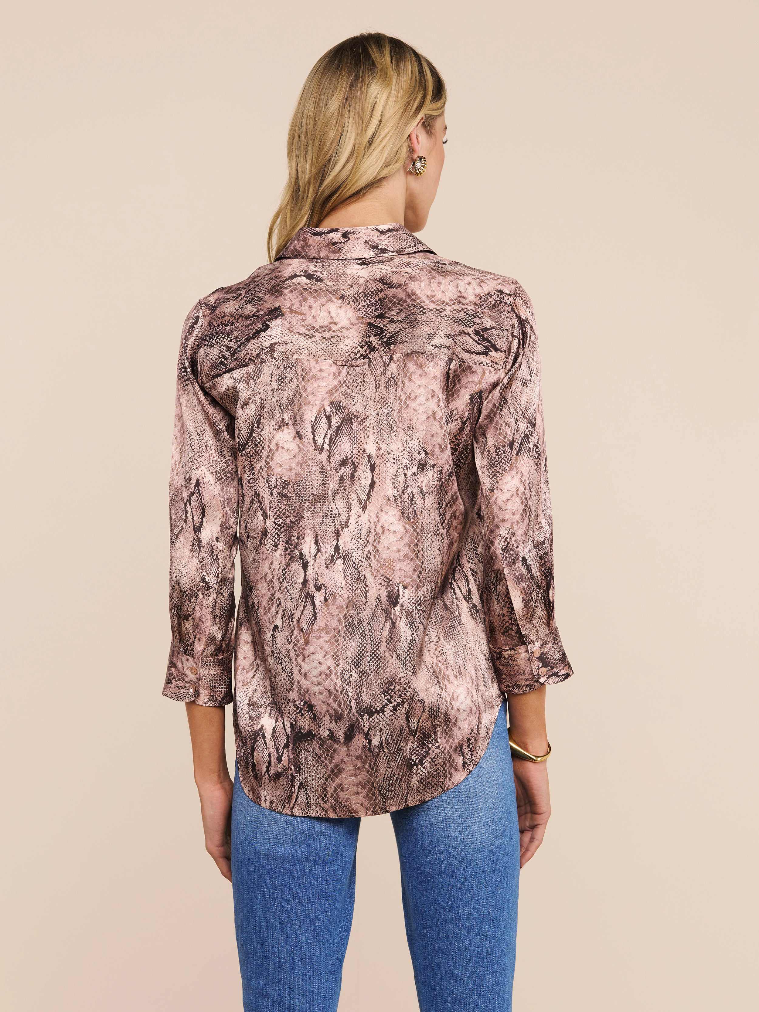A person with long blonde hair is shown from the back against a plain, light background, wearing the Dani Silk Blouse—a snake print top with three-quarter sleeves—paired with blue jeans.