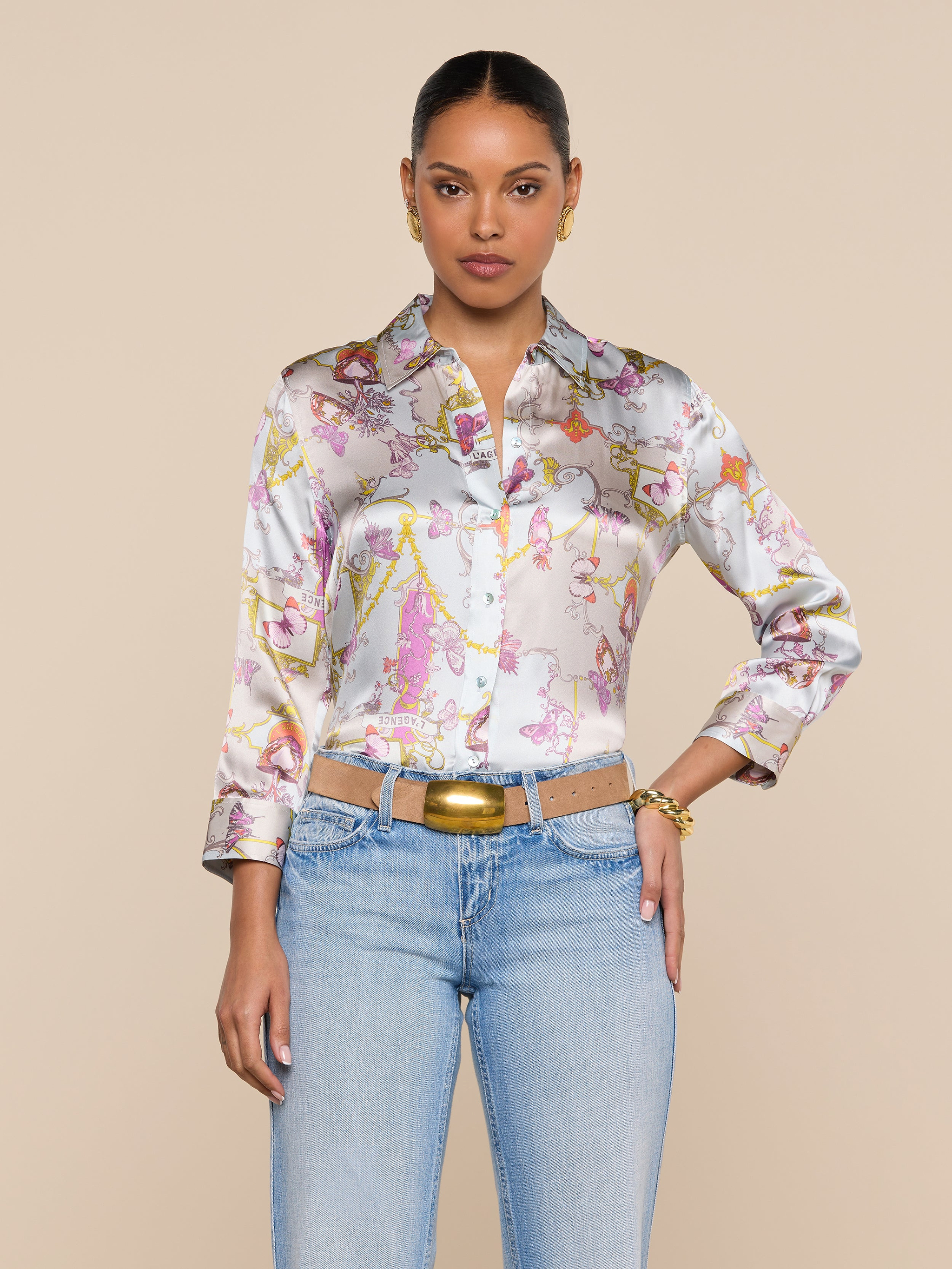 A woman wearing the Dani Silk Blouse paired with light blue jeans and a beige belt stands against a plain light background, looking directly at the camera with a neutral expression.