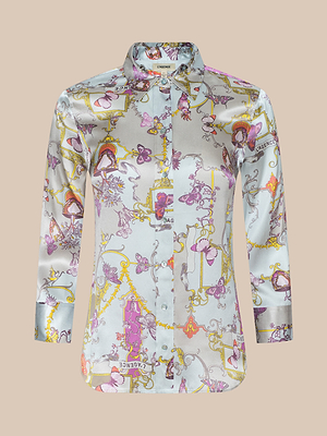 The Dani Silk Blouse is a long-sleeve, button-down shirt with a shiny pastel abstract print featuring florals, faces, and text accents in pink, purple, yellow, and white on light blue silk.