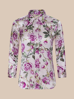 The Dani Silk Blouse is a long-sleeve, button-up top with a shiny satin finish, showcasing a purple and green rose print on light pink. It features a pointed collar and tailored fit for an elegant look.