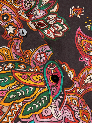 Close-up of the L'AGENCE Dani Silk Blouse, a women's slim-fit shirt with a vibrant paisley and floral print in pink, green, yellow, orange, and red on a dark background, finished with black and white buttons.