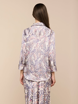 Una mujer de pelo largo y castaño, de espaldas, lleva la blusa de seda Dani, con estampado de alas de mariposa y mangas tres cuartos, y pantalones a juego, sobre un fondo beige.
