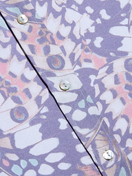 Primo piano del tessuto della blusa Dani Silk con motivi astratti ispirati alle ali delle farfalle in viola, rosa e bianco, bottoni iridescenti lungo la cucitura e una morbida finitura in seta per un look organico e ispirato alla natura.