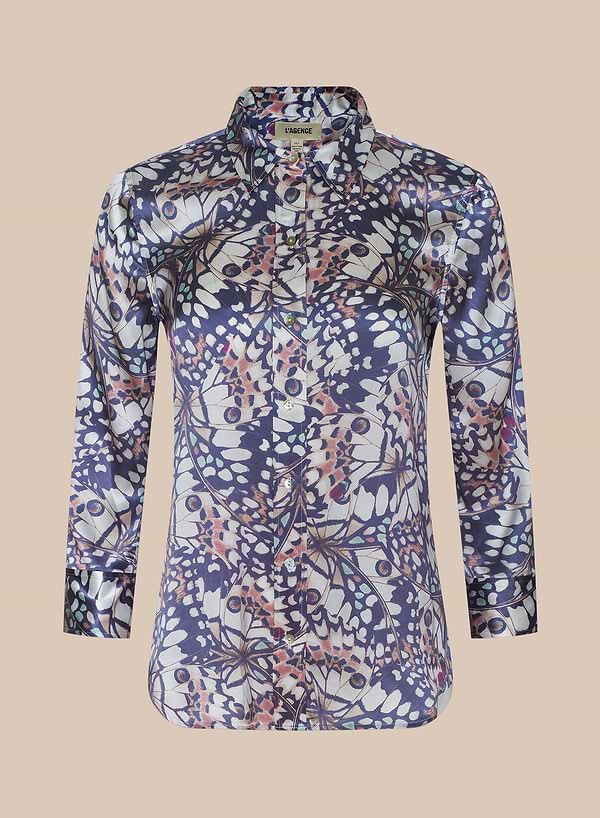 La blusa de seda Dani luce un vibrante estampado de alas de mariposa en tonos azul marino, rosa, blanco y beige sobre un fondo liso beige.