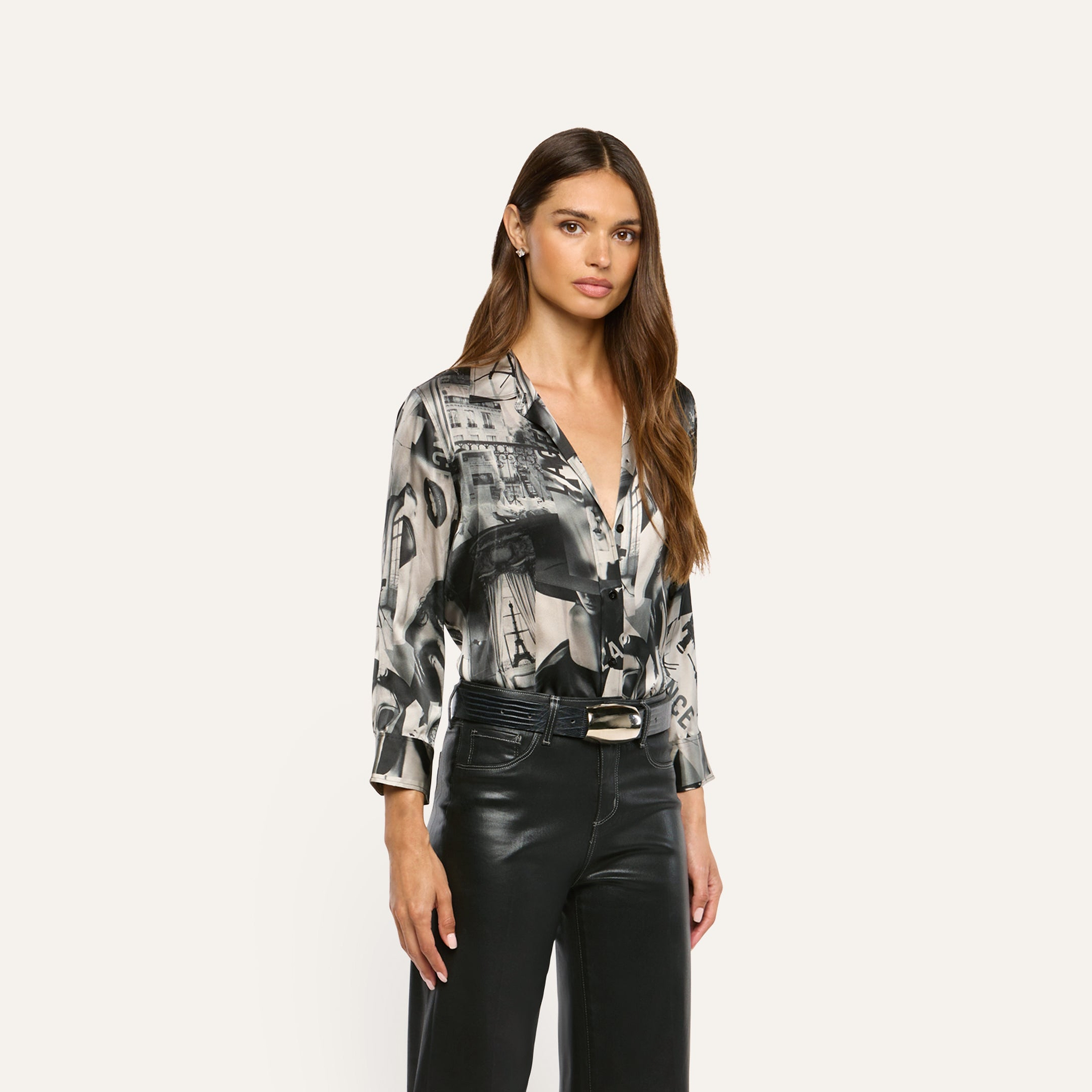 A woman wears a Dani Silk Blouse with a grey and black abstract architectural print, tucked into black pants with a belt.