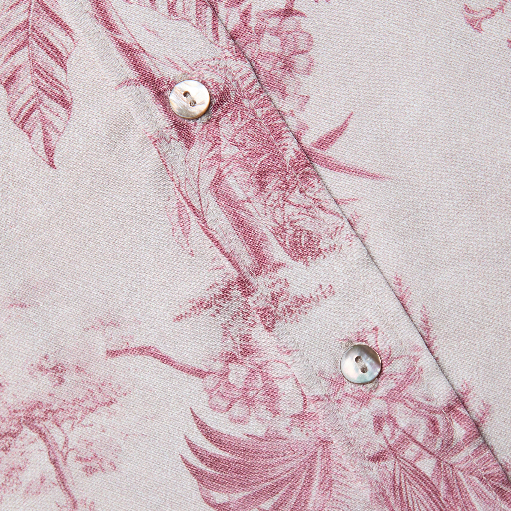 Nahaufnahme der Dani Silk Blouse, einer hellrosa Seidenbluse mit einem dunkelrosa Dschungel-Toile-Druck mit Vögeln und Blättern, zwei weißen Knöpfen und sichtbaren Nähten.