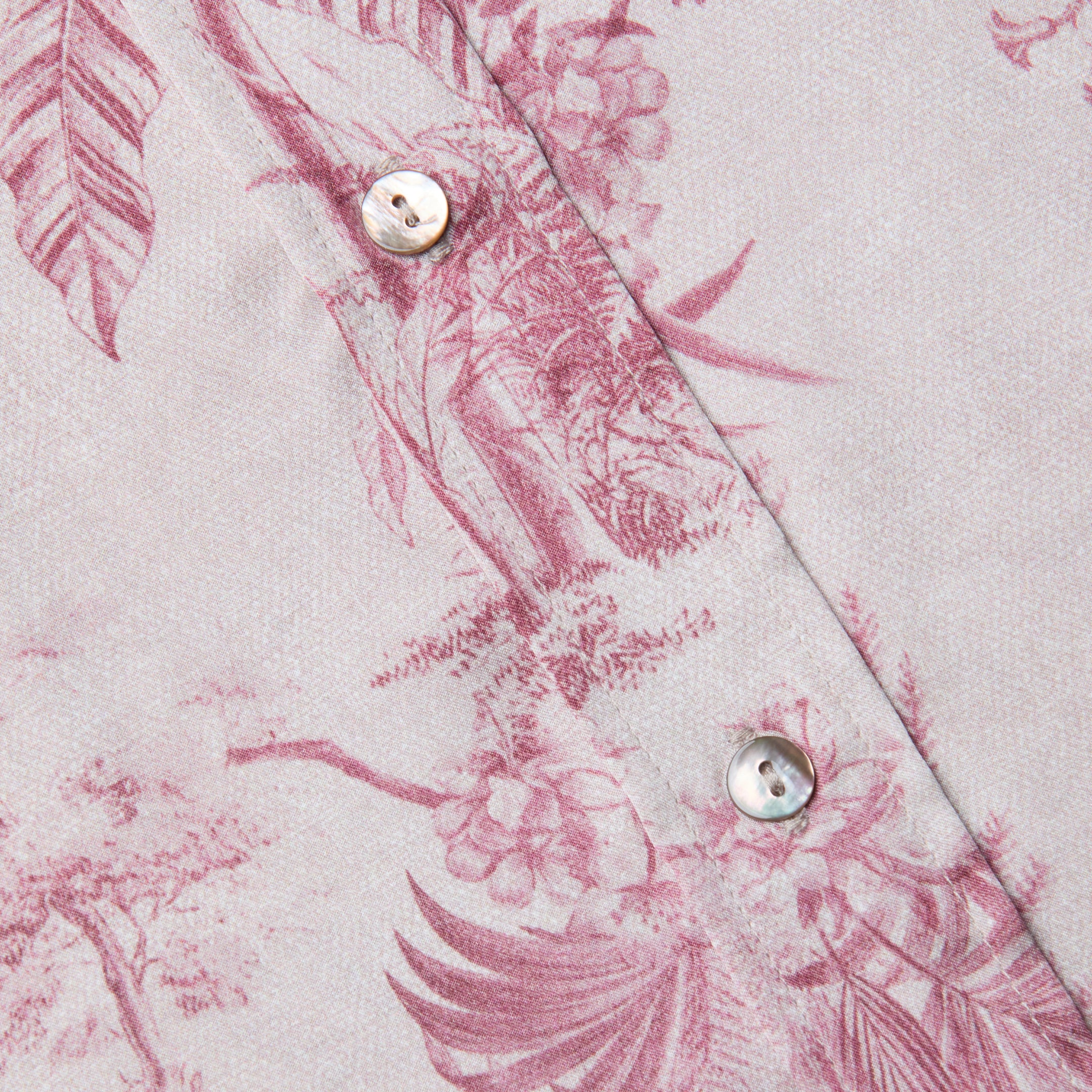 Nahaufnahme der Dani Silk Blouse, einer hellrosa Seidenbluse mit einem dunkelrosa Dschungel-Toile-Druck mit Vögeln und Blättern, zwei weißen Knöpfen und sichtbaren Nähten.