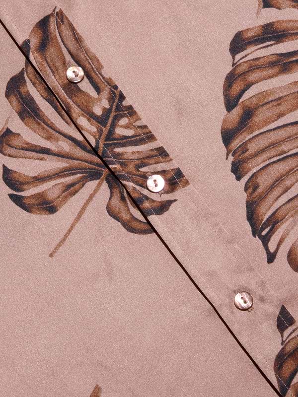 Close-up of the Dani Silk Blouse in beige, featuring a brown palm leaf print and pearl-like buttons. The smooth silk fabric and bold, tropical-inspired design give this button-down a distinctive look.