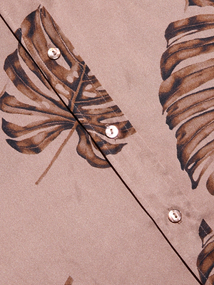 Close-up of the Dani Silk Blouse, showcasing its brown fabric with dark palm leaf print and light-colored buttons arranged along a diagonal seam.