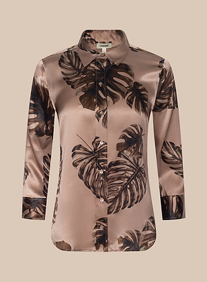 The Dani Silk Blouse is a silky, long-sleeve button-up with a brown and beige base and bold dark palm leaf print. It has a collar, slightly loose fit, and is shown on a plain light beige background.