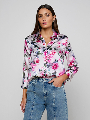 A woman wearing the Dani Silk Blouse, a long-sleeve button-down with a pink rose print, and high-waisted blue jeans stands against a plain light gray background.