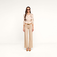 A woman wearing sunglasses, the Tyler Silk Blouse from L’AGENCE, beige wide-leg pants, and heels stands facing forward in a minimal white studio.