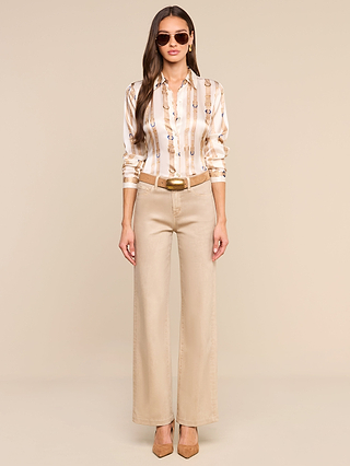 A woman wearing sunglasses, a L’AGENCE Tyler Silk Blouse with long sleeves and stripes, wide-leg beige pants with a belt, and tan heels stands against a plain beige background.