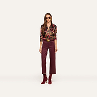A woman wearing sunglasses, the Tyler Silk Blouse from L’AGENCE—a colorful floral silk top—maroon pants, and matching maroon boots stands facing forward against a plain light background.