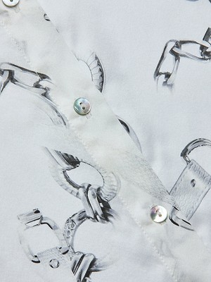 Close-up of the Tyler Silk Blouse, showcasing a gray chain print, metallic-look buttons, detailed stitching, and a smooth, slightly glossy finish.