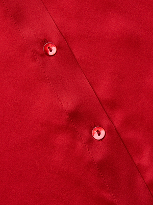 Close-up of the glossy red silk Tyler Blouse by L'AGENCE, showcasing smooth fabric and two round red buttons sewn along a seam with visible stitching.