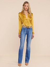 A woman stands against a plain white background wearing the shiny yellow Tyler Silk Blouse, blue jeans with a belt, and tan heels. She has long blonde hair and a neutral expression.