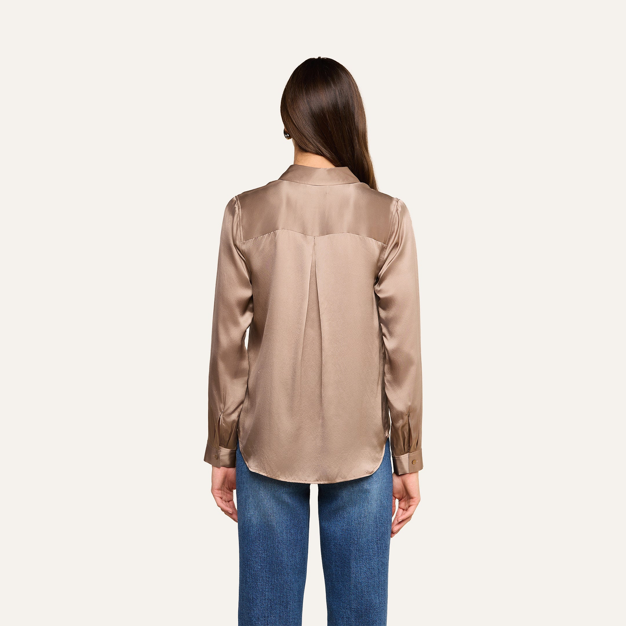 A woman with long brown hair, seen from behind, wears the Tyler Silk Blouse in shiny cardamom brown with long sleeves and blue jeans against a plain light background.