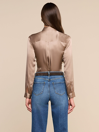 A woman with long brown hair is shown from the back, wearing the Tyler Silk Blouse in cardamom brown and blue jeans, standing against a plain beige background.