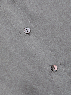 Close-up of the Tyler Silk Blouse in gray, highlighting a smooth long-sleeve fabric with a seam and two vertically aligned brownish buttons featuring a subtle sheen—signature details of this L’AGENCE bestseller.
