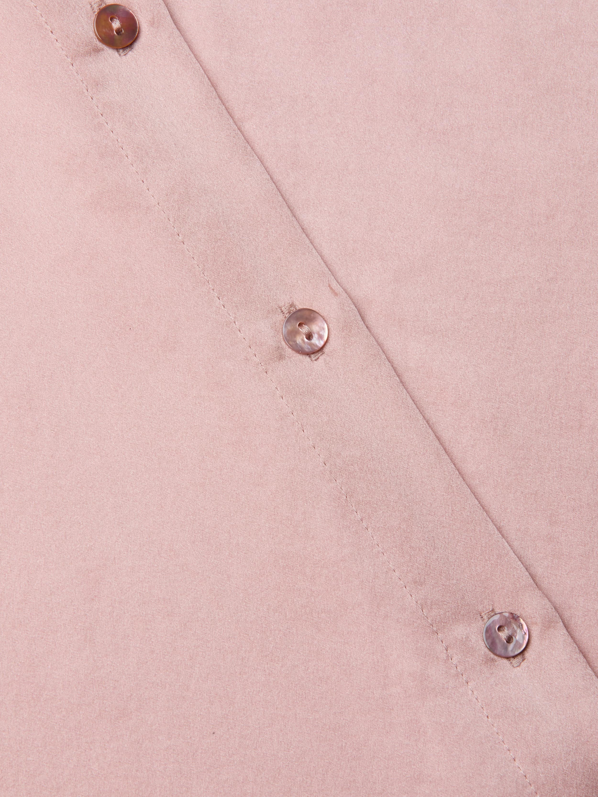 Close-up of the Tyler Silk Blouse in light pink, featuring three shiny round buttons arranged diagonally, showcasing its smooth silk texture and precise stitching along the edge.