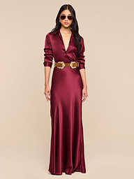 Woman wearing the Tyler Silk Blouse in merlot red silk charmeuse with a plunging neckline and a wide decorative belt, standing against a plain white background and wearing sunglasses.