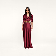Wearing sunglasses, the woman stands against a plain white background in the Tyler Silk Blouse and a long, merlot red silk charmeuse skirt with a gold belt.