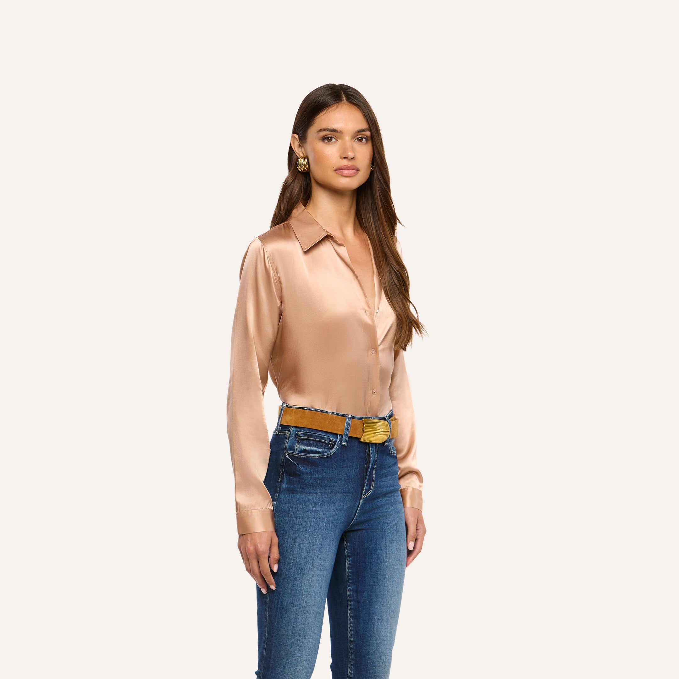 A woman wearing a tan L’AGENCE Tyler Silk Blouse tucked into blue jeans with a tan belt.