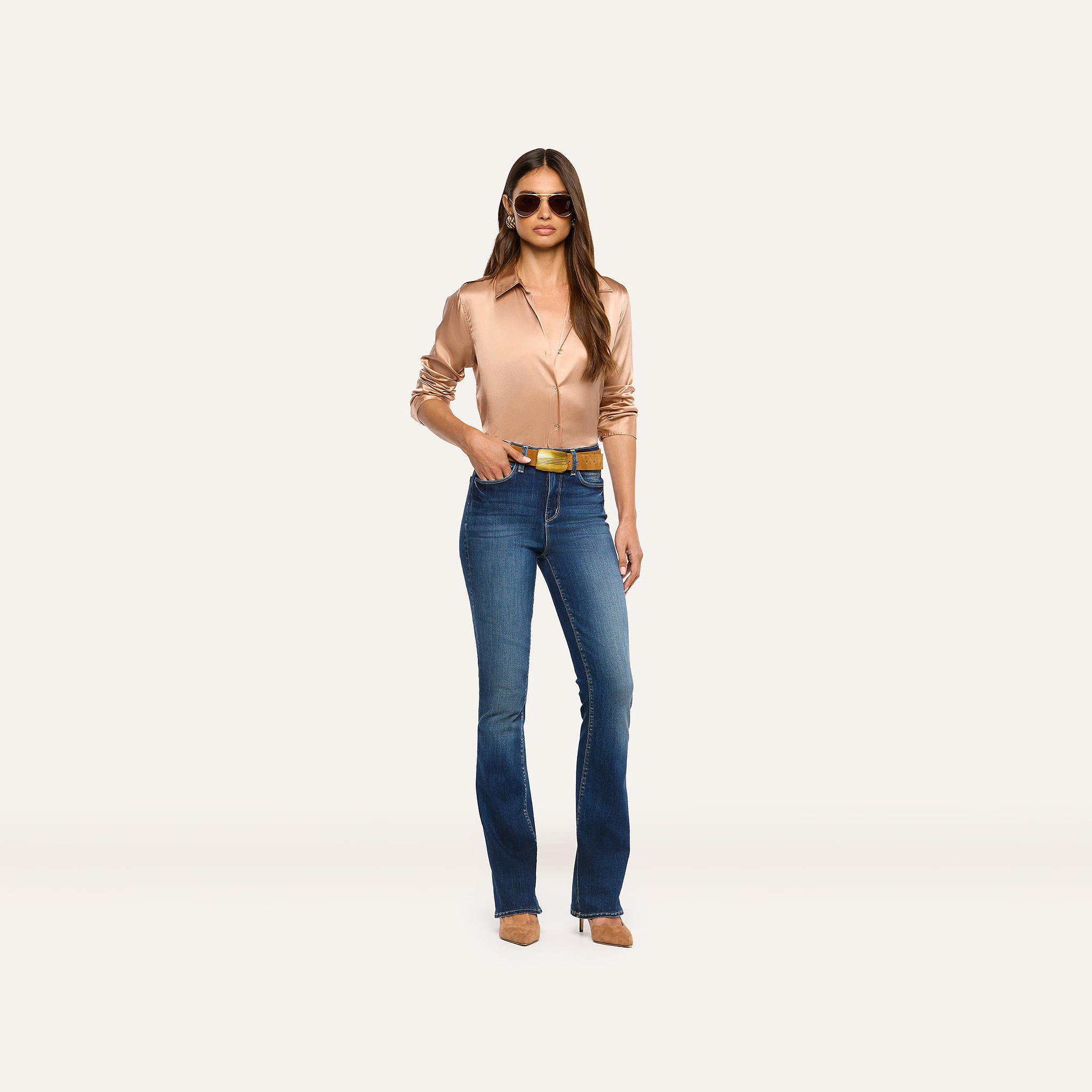 A person wearing a tan Tyler Silk Blouse, a gold belt, and blue flared jeans.