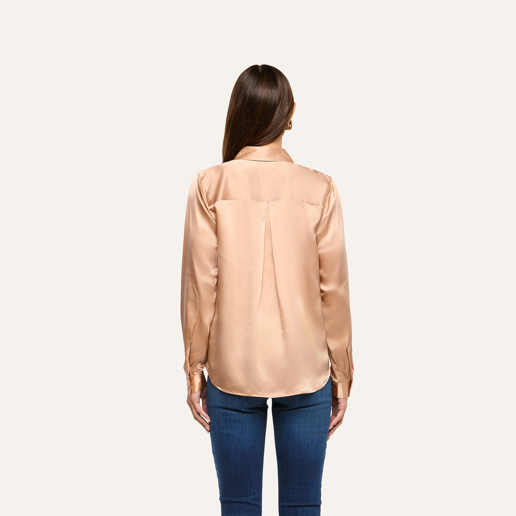 Back view of a person wearing a long-sleeve, champagne-colored L’AGENCE Tyler Silk Blouse and blue jeans.