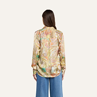 Eine Person mit langen braunen Haaren, von hinten gesehen, trägt vor einem beigen Hintergrund die farbenfrohe Tyler-Seidenbluse mit Paisley-Muster und eine blaue Jeans mit weitem Bein.