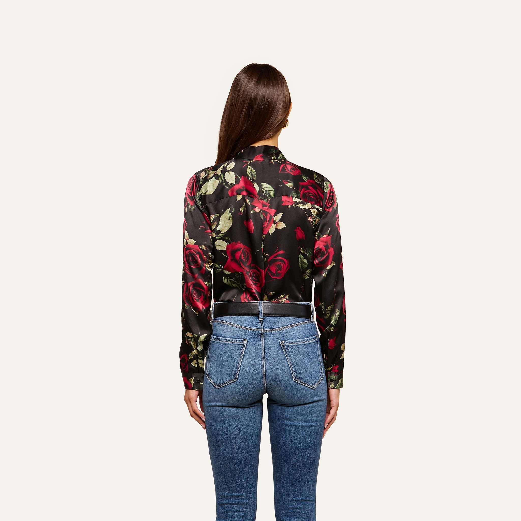 A woman with long brown hair, seen from behind, wears the Tyler Silk Blouse and blue jeans, standing against a plain light background.