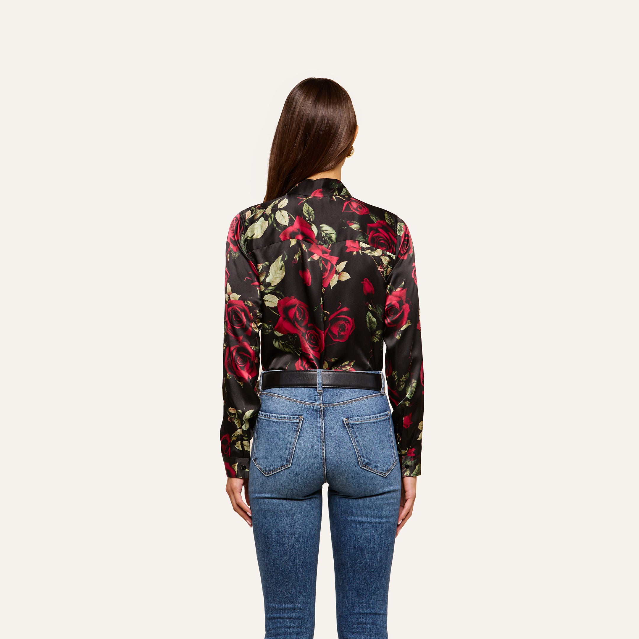 A woman with long brown hair, seen from behind, wears the Tyler Silk Blouse and blue jeans, standing against a plain light background.