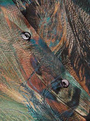 Close-up of the L'AGENCE Tyler Silk Blouse: features vibrant green, orange, and brown abstract feather prints on silk fabric with two black buttons sewn along the seam.