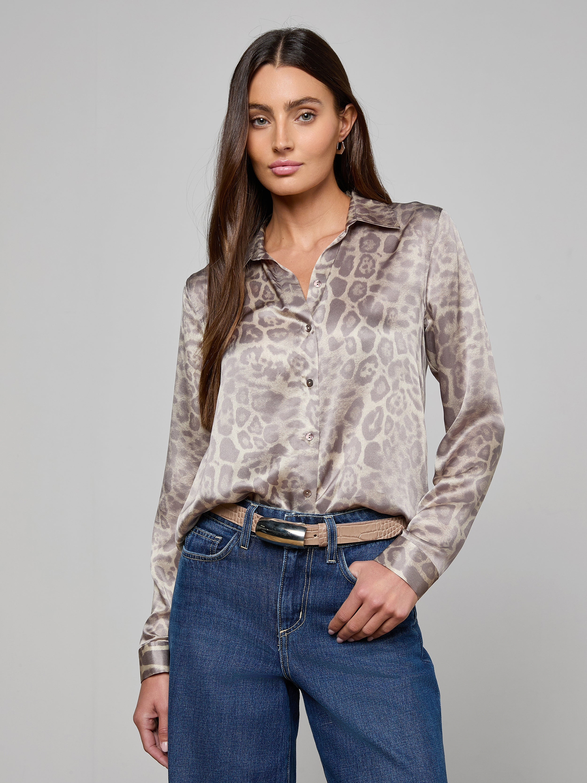 A woman stands with one hand in her pocket against a plain, light background, wearing a long-sleeve animal print blouse tucked into blue jeans and styled with the Marlowe Croc-Embossed Leather Belt.