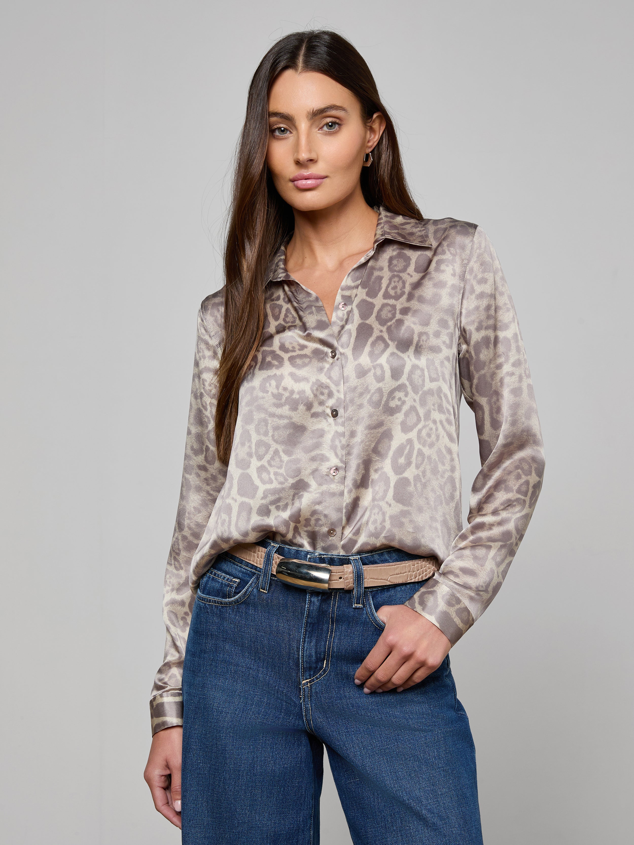 A woman stands with one hand in her pocket against a plain, light background, wearing a long-sleeve animal print blouse tucked into blue jeans and styled with the Marlowe Croc-Embossed Leather Belt.
